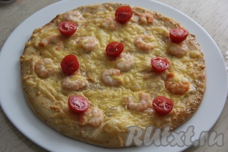 Горячую пиццу "Цезарь" с креветками переложить на тарелку для подачи и разложить сверху дольки помидоров черри.