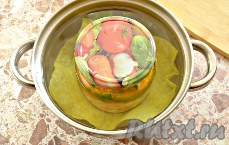 Банку накрываем (но не закручиваем) крышкой. Выкладываем на дно кастрюли тканевую салфетку (или полотенце, сложенное в 2-3 раза), сверху ставим банку с салатом. Вливаем горячую воду в кастрюлю, чтобы она доходила до плечиков банки. Кастрюлю с салатом ставим на средний огонь, а после того как вода в кастрюле закипит, уменьшаем огонь и готовим (стерилизуем) салат с морковью, огурцами и болгарским перцем 20 минут.