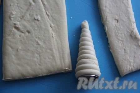 Намотать полоску теста, слегка растягивая её, на конус в виде спирали. Наматывать тесто нужно, начиная с широкой стороны конуса. Тесто должно при обматывании конуса ложиться слегка внахлёст. Низ будущей трубочки (её конец) закрыть тестом (это нужно для того чтобы, крем при наполнении трубочек из них не "вытекал"). Из каждого пласта теста получается 10-11 полосок.
