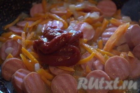Затем к обжаренному луку, моркови и сосискам добавить томатную пасту, перемешать.
