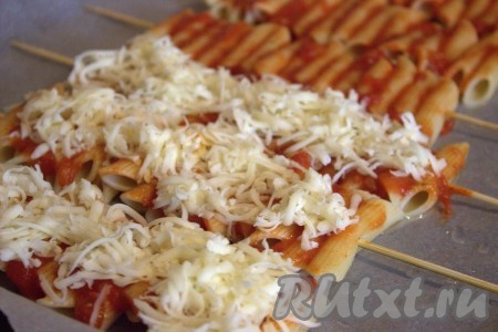 Противень застелить пергаментной бумагой, выложить на противень шпажки с макаронами. Сыр натереть на средней тёрке и разделить на две части. Посыпать шпажки с макаронами половиной натёртого сыра.