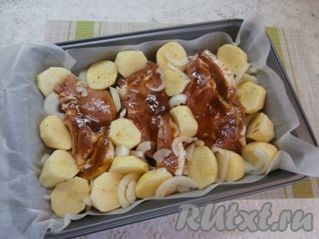 Далее картофель очистить, помыть и разрезать каждый клубень на 2-4 части, посолить и поперчить. Лук очистить от шелухи и нарезать на полукольца. Заполнить пустоты между стейками корейки подготовленным картофелем. Между картофелем и мясом разместить лук.