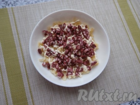 Копчёную колбасу нарезать небольшими кубиками и выложить вторым слоем.