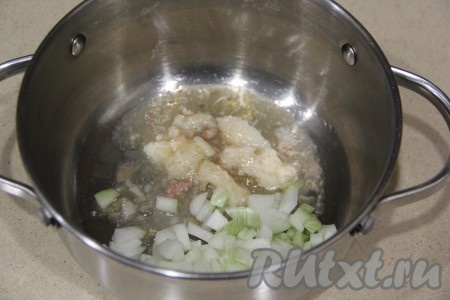 В кастрюлю с толстым дном выложить немного жира от тушёнки. Лук почистить, мелко нарезать и переложить в кастрюлю к жиру.