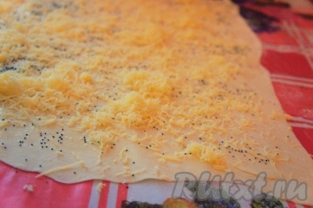 Посыпать тесто половиной натёртого сыра и маком. Свернуть плотным рулетом.