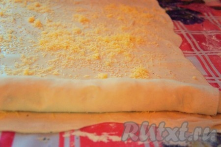 Вторую половину теста также тонко раскатать, смазать яйцом, посыпать оставшимся сыром и кунжутом. Выложить на пласт теста первый "рулет" и свернуть вместе плотным рулетом.