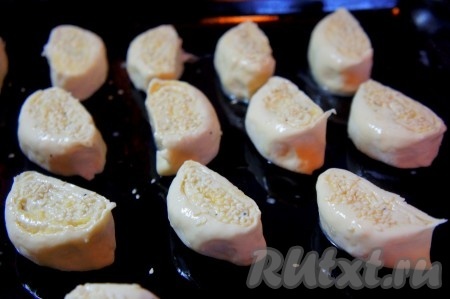 Противень смазать растительным маслом, выложить нарезанные ранее заготовки для сырных булочек, смазать их яйцом и присыпать кунжутом. 