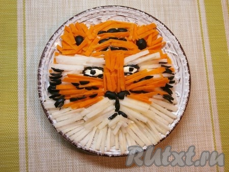 Выкладывать морковку и дайкон поверх салата в виде морды тигра, как на фото. Маслины использовать для оформления глаз, ушей, носа и полос тигра. В таком виде салат подать к столу.