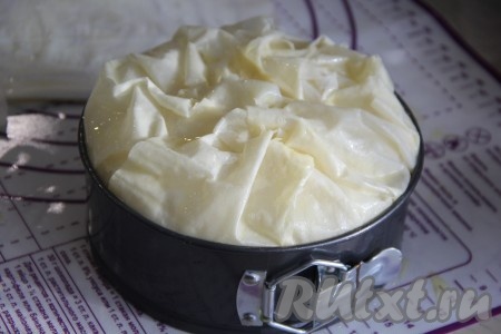 Повторить слои из начинки: оставшаяся половина фарша, присолить, оставшаяся смесь яйца и сметаны, оставшаяся часть сыра с зеленью, кружочки помидора и 25 грамм натёртого сыра. Все свисающие кончики теста фило завернуть поверх начинки в хаотичном порядке. Сформировать волны. Желток взбить и аккуратно смазать верх пирога желтком.