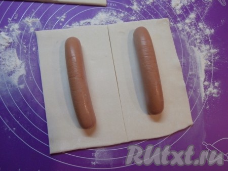 При комнатной температуре разморозить слоёное бездрожжевое тесто. На присыпанной мукой поверхности раскатать пласты размороженного слоёного теста. Толщина раскатанного теста должна быть не более 0,5 см. Разрезать раскатанное тесто на прямоугольники, их длина должна быть чуть длиннее сосисок, ширина - чтобы можно было сосиски завернуть.