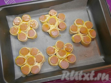 Смазать верх сосисок в тесте яичным желтком.