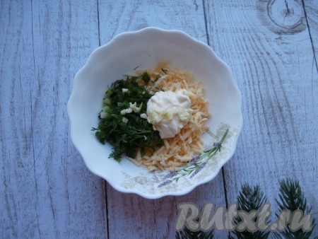 Сыр натереть на средней (или мелкой) тёрке, выложить в другую тарелку, добавить оставшуюся 1 столовую ложку майонеза, вторую половину мелко нарезанного зелёного лука и укропа, а также измельчённый зубчик чеснока.
