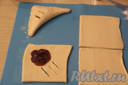 Каждый пласт слоёного теста разрезать на 4 квадрата. Каждый квадрат мысленно поделить по диагонали на две половины. На одну половину квадрата выложить столовую ложку смеси малинового варенья и крахмала, на второй половине квадрата сделать 3 разреза, как на фото. Накрыть тестом начинку и хорошо скрепить края. У нас получатся треугольные слойки. Края слоек скрепить с помощью вилки. У меня получилось 8 слоек с вареньем.