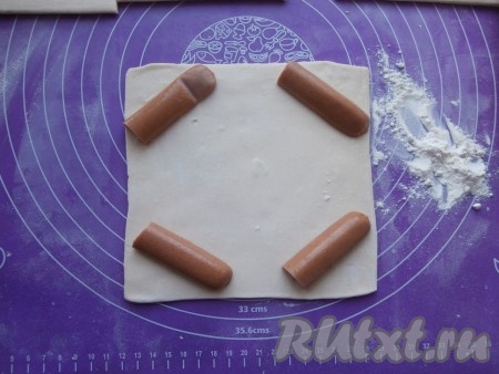 Каждый квадрат на припылённой мукой поверхности раскатать так, чтобы его размер был 16 см х 16 см. По углам выложить сосиски, разрезанные пополам, а затем - ещё на 2 части (то есть для каждого хачапури нужна будет одна сосиска). 