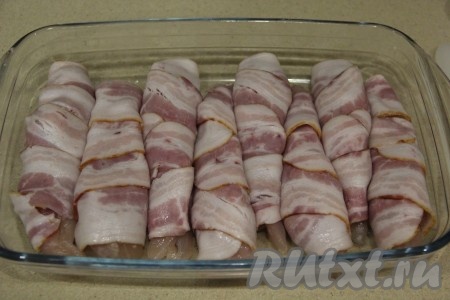 Кусочки филе слегка посолить. Каждый кусочек куриного мяса плотно завернуть в полоску бекона. Выложить куриное филе, завёрнутое в бекон, в жаропрочную форму. Заготовки в форме должны лежать достаточно плотно.