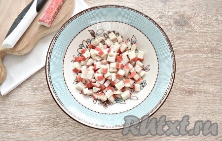 Прежде всего отвариваем яйца вкрутую (варим после закипания воды 8-10 минут), остужаем их в ледяной воде и очищаем. Если крабовые палочки заморожены, им нужно дать разморозиться при комнатной температуре. Удаляем с крабовых палочек упаковку, а затем нарезаем их на небольшие кубики и перекладываем в достаточно глубокую тарелку (или миску).