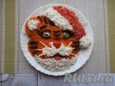 Отварную морковь натереть на мелкой тёрке и покрыть морковкой всю поверхность салата. Шапочку выложить из нарезанного кубиками свежего помидора. Опушку, помпон, ушко, часть носа и низ мордочки оформить натёртыми на средней тёрке белками. Глаза сделать из кружочков маринованного огурца. Носик и ротик - из помидора, усы - из тонких кусочков сыра. Полосочки, зрачки, обводка глаз - из чёрных маслин (часть из полосочек, часть - из натёртых маслин).