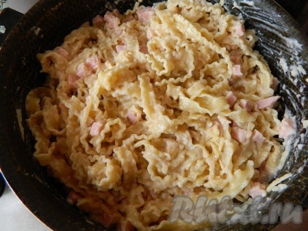 Сваренную и промытую лапшу перекладываем в форму для запекания, смазанную сливочным маслом, добавляем соус, ветчину и 150 грамм сыра. Все хорошо перемешиваем.