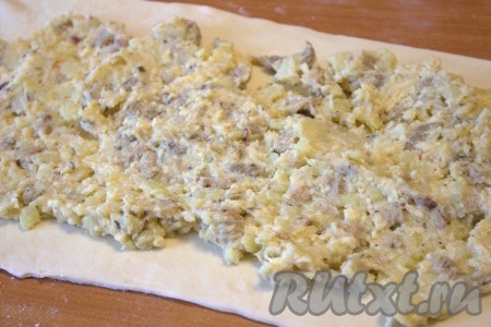 Рабочую поверхность припылить мукой, размороженное слоёное тесто раскатать в один пласт толщиной 2-3 миллиметра (у меня получился пласт размером 30 см на 50 см). Я делала один длинный пирог, но можно с таким же успехом сделать два пирога меньшего размера, разделив тесто на два пласта. Выложить картофельно-мясную начинку на раскатанное слоёное тесто, немного отступив от краёв.