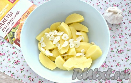 Очищенные зубчики чеснока нарезаем на пластины и выкладываем к картофельным долькам.