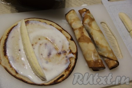 Каждый блин смазать сметанным кремом и выложить брусок банана. Я бананы разрезала на 4 части вдоль. Скрутить блин с начинкой в плотный рулетик.