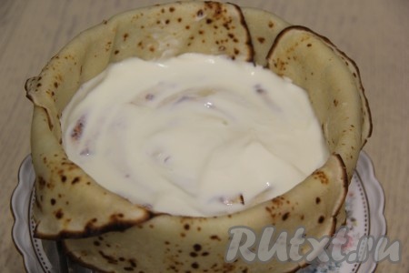 Выложить второй слой блинных рулетиков улиткой и обильно смазать верх кремом.