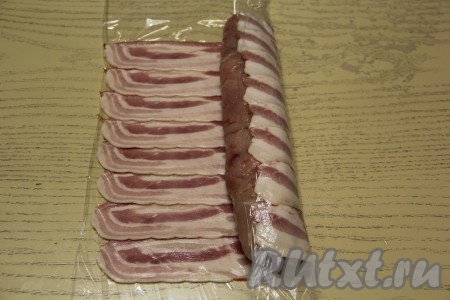 С куриного рулета аккуратно снять пищевую плёнку. Выложить куриный рулет на край бекона и завернуть его в слой бекона, помогая себе формировать рулет в беконе с помощью пищевой плёнки. Не заворачивайте пищевую плёнку вместе с беконом, а аккуратно её снимайте с завёрнутого края. Конечно же запекать рулет мы должны без плёнки.