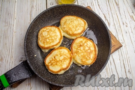 Перед выпечкой обязательно перемешивайте тесто. На сковороде хорошо прогрейте немного растительного масла, выкладывайте по столовой ложке теста в виде круглых оладий. Оладьи нужно выкладывать на некотором расстоянии друг от друга, так как они немного увеличатся в процессе выпечки. Жарьте оладьи на среднем огне до золотистого цвета (2-3 минуты), затем переверните на другую сторону, накройте крышкой и продолжайте жарку ещё 2 минуты. Переложите готовые оладьи со сковороды на бумажное полотенце для удаления лишнего масла. Аналогично пожарьте все оладушки.
