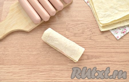 На каждую заготовку с краю кладём сосиску и заворачиваем её в лаваш. Также поступаем с оставшимися сосисками.