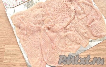 На столе расстилаем кусок фольги, сложенный вдвое. Распределяем на фольге отбитые пласты куриного филе немного внахлёст, формируя четырёхугольную заготовку. У меня получилась заготовка размером 25 сантиметров на 30 сантиметров.