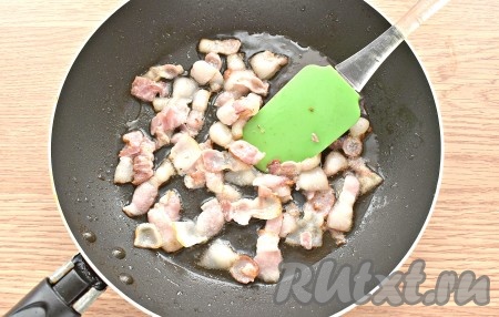 На сковороде разогреваем оливковое масло. Если такое масло отсутствует, подойдёт и подсолнечное масло. Выкладываем на сковороду кусочки бекона и обжариваем их, периодически перемешивая, 2-3 минуты на среднем огне.