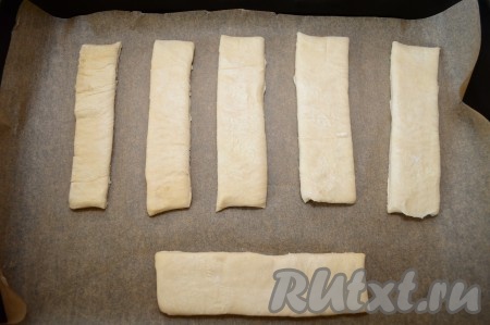 При помощи острого ножа разрезать тесто на прямоугольные полоски (язычки). Из одного пласта теста у меня вышло 6 язычков. Застелить противень бумагой для выпечки. Если вы сомневаетесь в качестве бумаги, то лучше дополнительно промазать поверхность бумаги растительным маслом. Я использую качественную бумагу для выпечки, в состав которой входит силикон. К такой силиконизированной бумаге ничего не пристаёт, поэтому я маслом её не смазываю. Выложить язычки из слоёного теста на бумагу.