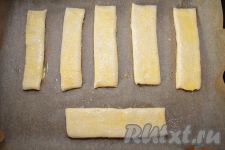 При помощи кулинарной кисти смазать верх язычков сырым яйцом. А потом посыпать слойки сверху сахаром. Я добавляю 3 чайные ложки сахара на 250 грамм слоёного дрожжевого теста, при этом язычки получаются сладкими, но в меру.