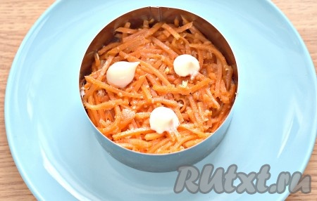 Морковку по-корейски отжимаем от пикантного маринада. Если полоски морковки длинные, тогда разрезаем их на несколько частей. Равномерно выкладываем морковку следующим слоем, немного утрамбовываем. Покрываем морковный слой майонезом.