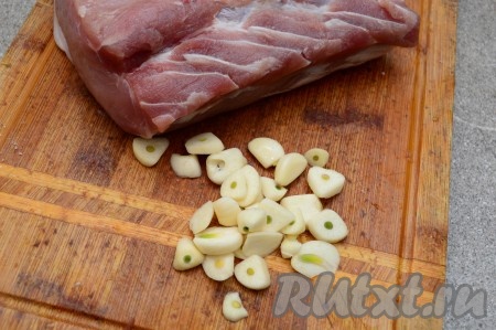 Для запекания идеально подходит свежая свиная корейка, но если у вас замороженное мясо, тогда его следует полностью разморозить. Лучше всего размораживать мясо медленно, тогда оно в процессе разморозки теряет меньше жидкости и после запекания остаётся более сочным. Для этого достаньте мясо из морозилки, поместите в глубокую миску (при разморозке будет выделяться вода, которая и будет сливаться в миску), поставьте на верхнюю полку холодильника и оставьте его до полного размораживания (обычно килограмм корейки полностью размораживается в течение одного дня). Когда корейка полностью разморозится, можно приступать непосредственного к приготовлению блюда. Прежде всего почистить от шелухи две головки чеснока. Одну головку чеснока нарезать на дольки (как на фото), а вторую - пока отложить в сторону.