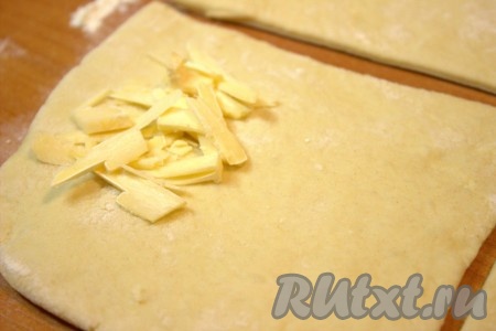 На каждую квадратную заготовку теста выложить ближе к одному из краёв, примерно, по одной столовой ложке натёртого сыра.