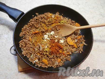 Затем в сковороду с овощами всыпать заранее промытую гречневую крупу, добавить соль, паприку, чёрный молотый перец и нарезанный на дольки чеснок, перемешать и обжарить, помешивая, в течение 2-3 минут.