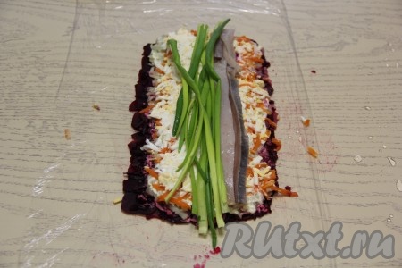 Затем выложить слой натёртой моркови, слегка смазать майонезом. Поверх морковки равномерно разложить натёртое яйцо. Этот слой майонезом можно не смазывать, ведь если будет много майонеза, рулет потечёт. Ближе к краю, противоположному от чистого края прямоугольника, выложить длинные брусочки селёдки и перья зелёного лука, как на фото. 