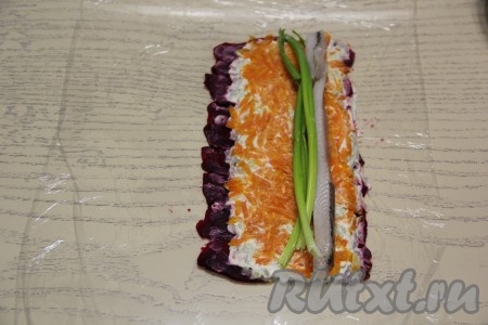 Филе сельди разрезать на длинные брусочки. Выложить брусочки селёдки ближе к краю, который является противоположным от свободного края (см. на фото). Рядом с селёдочкой выложить пару перьев зелёного лука.