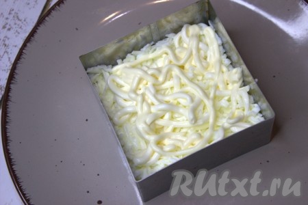 Выложить первым слоем половину белков, смешанных с плавленым сыром, слегка утрамбовать, сделать майонезную сеточку.