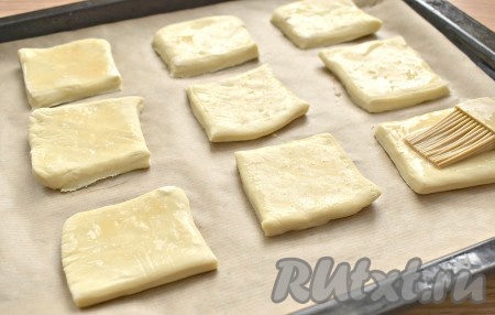 Половину квадратов (9 штук) сразу перекладываем на противень, который рекомендую застелить пергаментом. Смазываем заготовки взбитым яйцом.