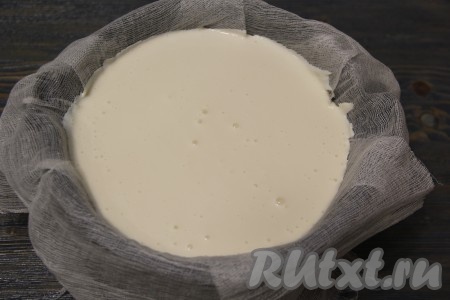Сито (или дуршлаг, или специальную форму для приготовления сыра) выстелить марлей, сложенной в несколько слоёв. Нужно не менее 3-4 слоёв марли. Края марли должны свисать с краёв формы. Аккуратно вылить массу в застеленную форму. Поставить форму с молочной массой над глубокой миской, куда будет стекать жидкость.