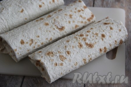 Завернуть начинку в лаваш в виде плоского рулета, сперва подвернув боковые края. Аналогично сформировать ещё 2 шаурмы.