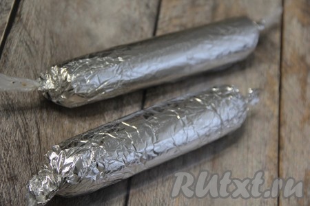 Колбаску из печенья и шоколада завернуть в плёнку, а затем в фольгу и прокатать по столу для придания более ровной формы. Таким же образом сформировать вторую шоколадную колбаску. Поместить колбаски в холодильник на пару часов.