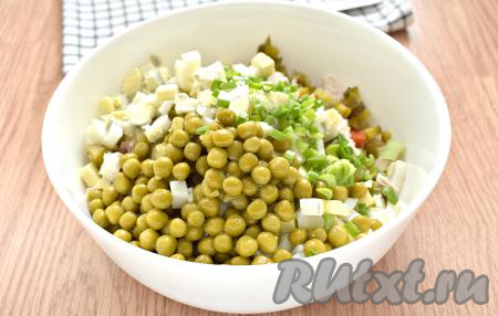 Откидываем зелёный консервированный горошек на сито, чтобы убрать лишнюю жидкость. Зелёный лук нарезаем мелко и вместе с горошком добавляем в салатник.