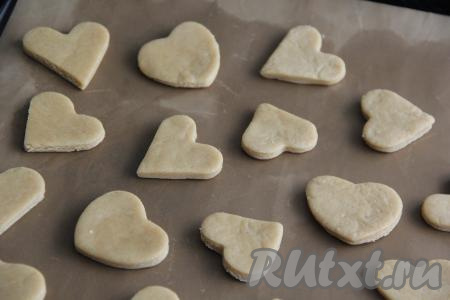 По истечении времени на присыпанной мукой поверхности песочное тесто раскатать в пласт толщиной, примерно, 0,5 см и с помощью формочек вырезать печенье в виде сердечек. Если нет формочек, то можно аккуратно вырезать сердечки острым ножом. Выложить заготовки печенья на противень, застеленный бумагой для выпечки (или тефлоновым ковриком).&nbsp;