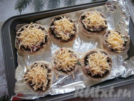 Сверху посыпать фаршированные грибы натёртым сыром.