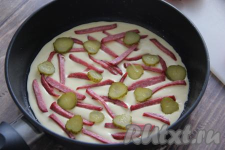 Поверх теста разложить кусочки колбасы и кружочки огурца.