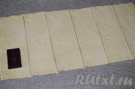 Размороженное слоёное тесто (у меня размер пласта теста был 14 см на 21 см) раскатать на слегка присыпанной мукой поверхности в прямоугольник размером 18 см на 42 см. Разделить раскатанное слоёное тесто на прямоугольники (размер прямоугольника зависит от длины и ширины долек шоколада). У меня дольки были достаточно большими (вес каждой дольки 15 грамм), поэтому я раскатанное тесто разделила на 6 прямоугольников (то есть мы будем формировать 6 слоек).