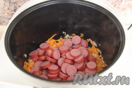 Когда обжаренные овощи станут мягкими, выложить к ним сосиски, очищенные от плёнки и нарезанные на кружочки. Перемешать сосиски с овощами.